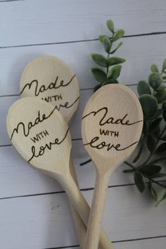 three wooden spoons with handwritten names on them sitting next to some green leaves