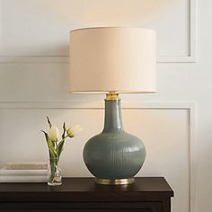 a green vase sitting on top of a wooden table next to a lamp and flowers