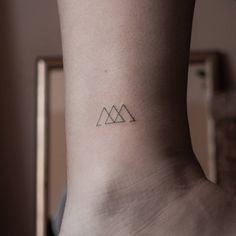 a small triangle tattoo on the back of a woman's left leg, with mountains in the background