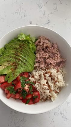 a white bowl filled with rice, meat and veggies next to an avocado