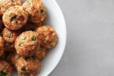 a white bowl filled with meatballs on top of a gray countertop next to a knife