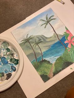 a painting is being displayed next to a white plate with flowers and palm trees on it