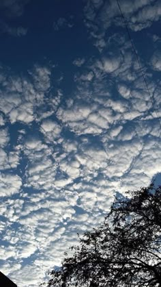 the sky is filled with many clouds and there are some trees in front of it