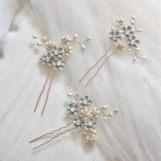 two bridal hair pins with flowers and pearls on top of a white fabric background