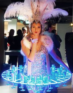 a woman in a feathered headdress is posing for the camera with many glasses