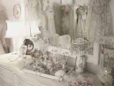 a white dresser topped with lots of different types of dresses and accessories next to a mirror