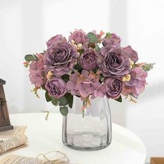 a vase filled with purple flowers sitting on top of a table next to an open book