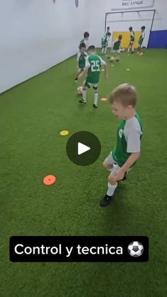 a little boy standing on top of a green field next to a soccer ball in the air