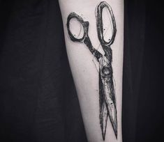 a tattoo with scissors and magnifying glass on the arm that is black and white