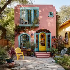 a pink house with blue shutters and yellow chairs on the front porch, surrounded by greenery