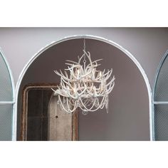 a white chandelier hanging from the ceiling in front of an arched doorway and mirror