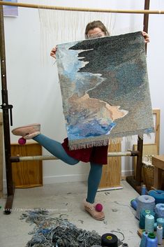 a woman holding up a piece of art with her feet in the air while standing on one leg