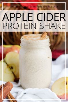 an apple cider protein shake in a mason jar with cinnamon sticks and apples around it