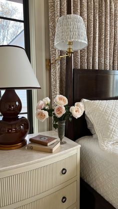 a bedroom with a lamp, bed and flowers on the nightstand next to the window