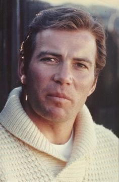 a man wearing a white sweater looking at the camera with a serious look on his face