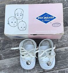 a pair of white baby shoes sitting on top of a wooden floor next to a box