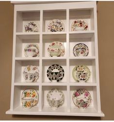 a white shelf filled with lots of plates on top of each other in front of a wall