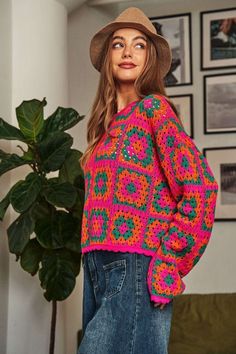 a woman wearing a colorful sweater and hat standing next to a potted plant in a living room