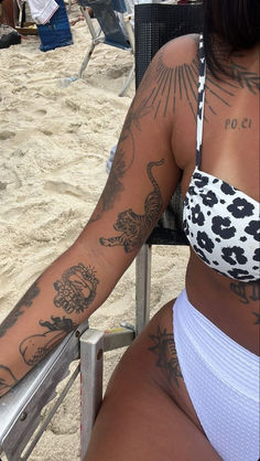 a woman sitting in a chair on the beach with tattoos on her arm and chest