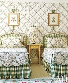 two beds in a room with floral wallpaper on the walls and green bedding