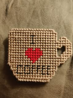 a knitted coffee cup with a red heart in the middle on a brown blanket