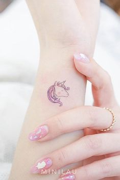 a woman's hand with a small unicorn tattoo on her left wrist and pink nail polish