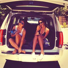 two young women sitting in the back of a white van with their feet on the trunk