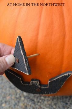 a hand holding a piece of wood in front of a pumpkin with the words at home in the north west on it