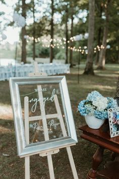 an easel with flowers and pictures on it sitting in the grass next to a wooden table