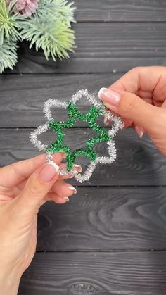 two hands are holding green and white string art pieces on a wooden table next to some plants