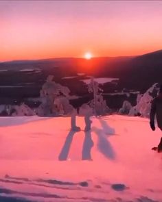 a man riding a snowboard down a snow covered slope at sunset with the sun behind him