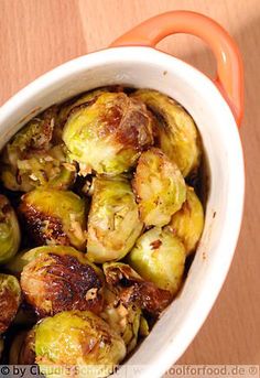 brussel sprouts in a white bowl with an orange handle on a wooden table