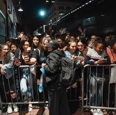 a group of people standing in front of a metal barricade with their cell phones