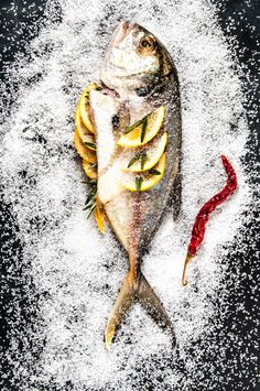 a fish with lemon slices and spices on it's side in the middle of powdered sugar