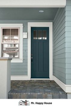 a blue front door on a green house with white trim and window sill in the foreground