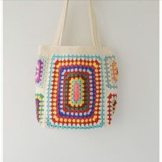 a multicolored crocheted bag hanging on the wall next to a white wall