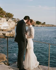 a bride and groom are kissing on the dock by the water at their wedding day