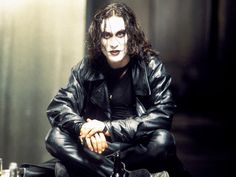 a man sitting on the ground with his arms crossed, wearing black leather clothes and holding a wine bottle