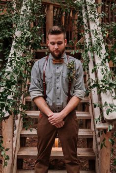 a man wearing suspenders and bow tie standing in front of stairs with greenery