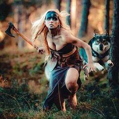 a woman dressed as a warrior running through the woods with an ax in her hand