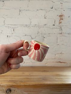 a hand holding a coffee cup on top of a wooden table next to a brick wall