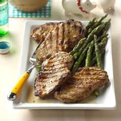 grilled meat and asparagus on a white plate with a yellow handled knife