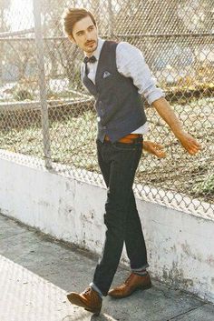 the man is walking down the street wearing a vest and bow tie with his hand in his pocket