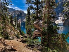 there is a trail going up the side of a mountain with blue water and mountains in the background