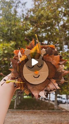 a person holding up a fake lion head with leaves on it's face in front of some trees