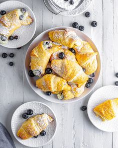 croissants with blueberries and powdered sugar are on plates next to other pastries