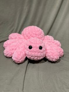 a pink stuffed animal laying on top of a gray sheet with eyes and ears sticking out