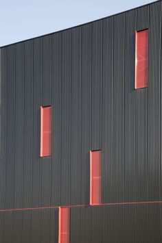 two red windows are on the side of a black building that is made out of corrugated