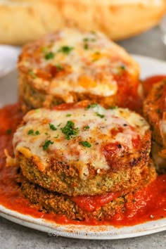 three meat patties on a plate with sauce and parmesan bread in the background