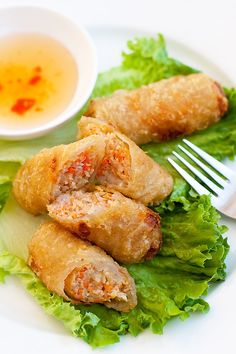 a white plate topped with meat and lettuce next to a bowl of dipping sauce